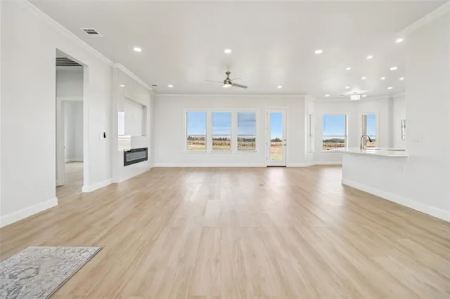 a view of an empty room with wooden floor and a kitchen