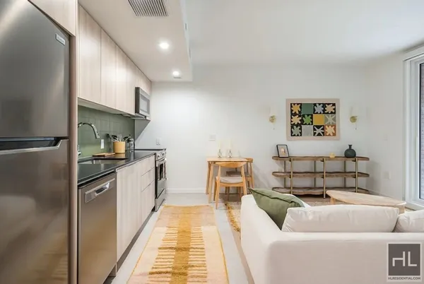 a living room with stainless steel appliances furniture a rug and a refrigerator
