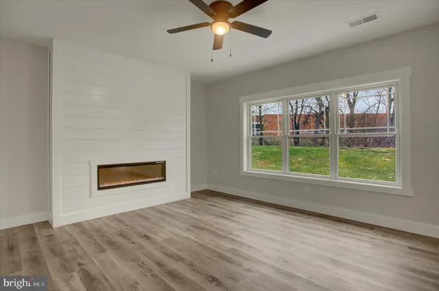an empty room with wooden floor chandelier fan and windows