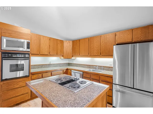 a kitchen with stainless steel appliances granite countertop a refrigerator a stove and a sink with wooden cabinets