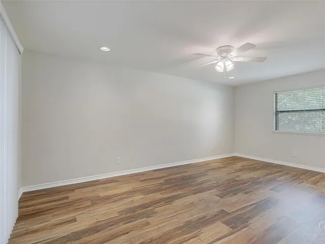 an empty room with wooden floor fan and windows