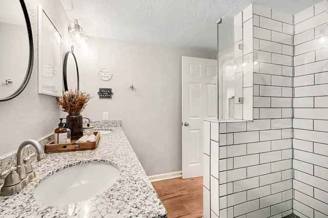 a bathroom with a granite countertop sink a mirror and shower