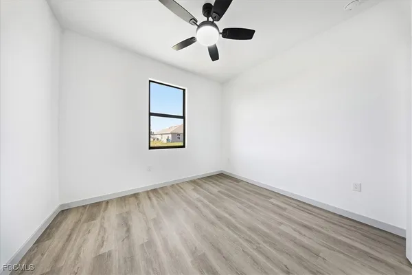an empty room with wooden floor chandelier fan and windows