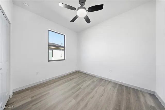 an empty room with wooden floor ceiling fan and windows