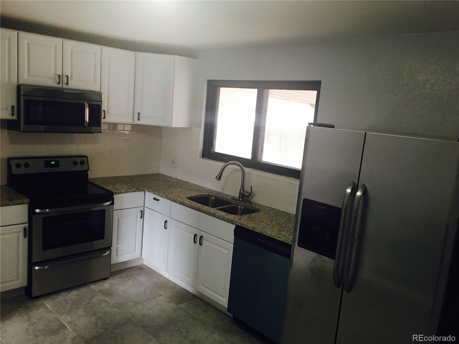 5542 Scranton Street Denver, CO 80239 - Photo 4 of 16 a kitchen with granite countertop a refrigerator stove and microwave