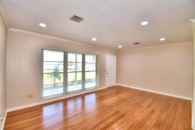 a view of an empty room with wooden floor and a window