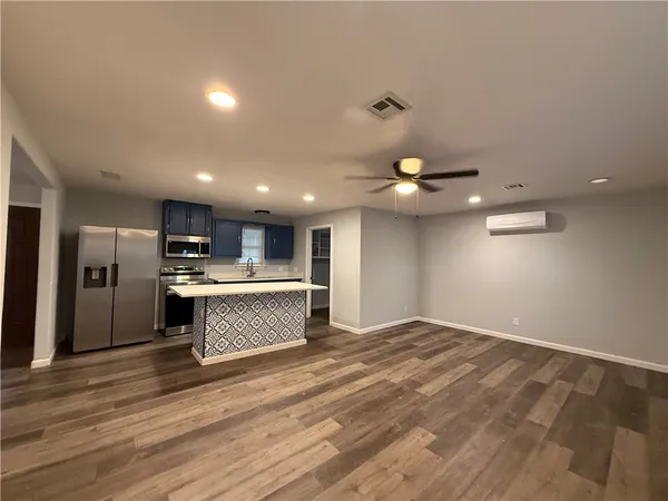 an empty room with wooden floor and kitchen view