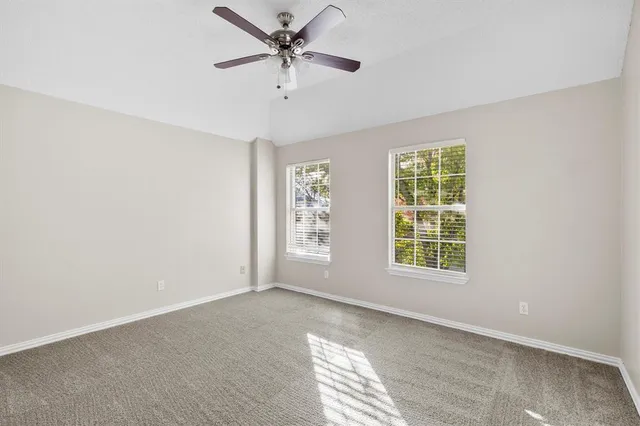 an empty room with chandelier fan and windows