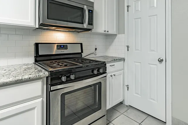 a kitchen with stainless steel appliances granite countertop white cabinets and a stove top oven