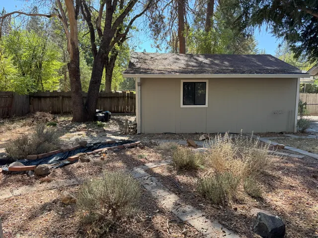 a backyard of a house with large trees and wooden fence