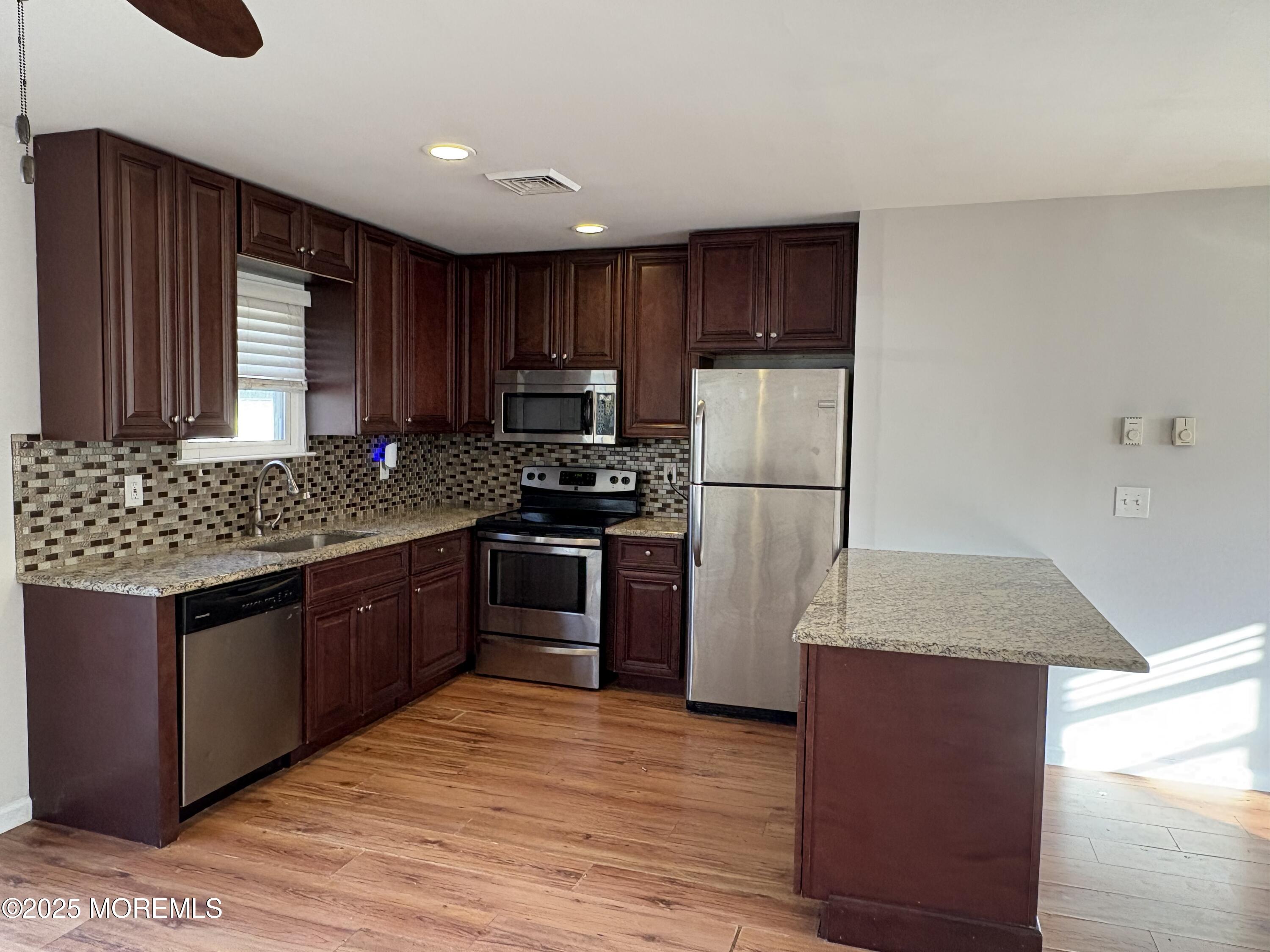 4 A Primrose Lane Jackson, NJ 08527 - Photo 2 of 14 a kitchen with granite countertop wooden cabinets a stove top oven a refrigerator and dishwasher with wooden floor
