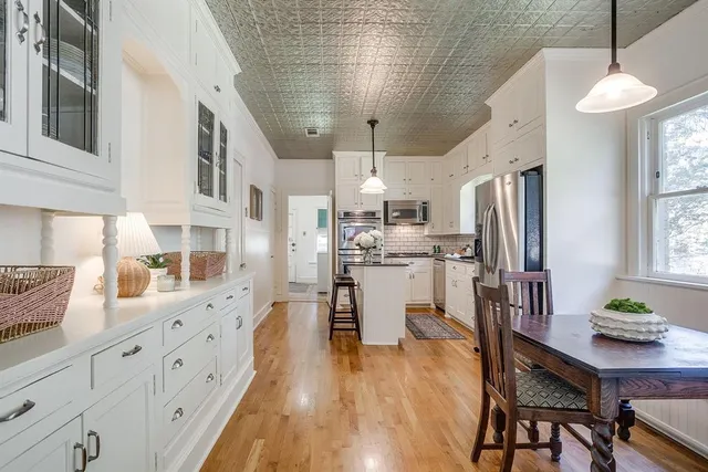 a large kitchen with white cabinets a counter space dining table and a large window