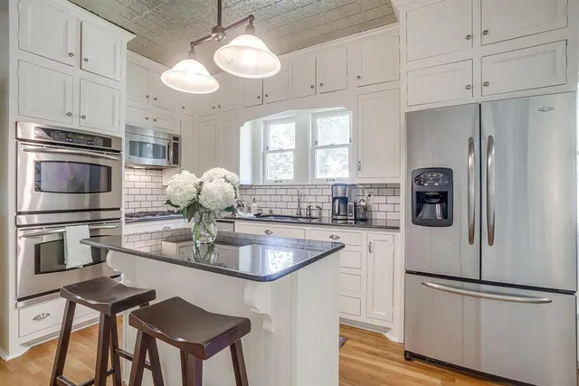 a kitchen with stainless steel appliances granite countertop a refrigerator a stove a sink and white cabinets