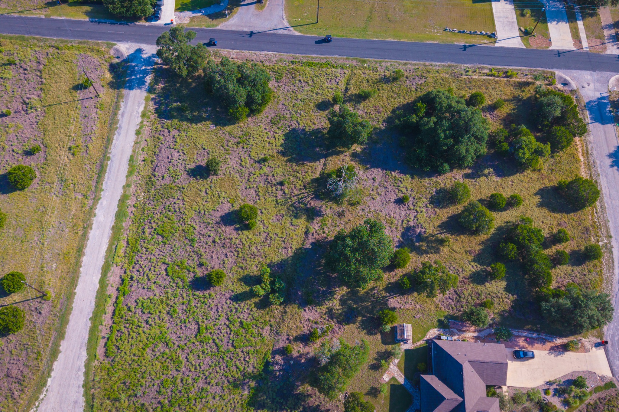 Lot 380 South Calvin Barrett Road Blanco, TX 78606 - Photo 10 of 24 A verdant, undeveloped land parcel offers ample space for building dreams, bordered by paved and unpaved roads.