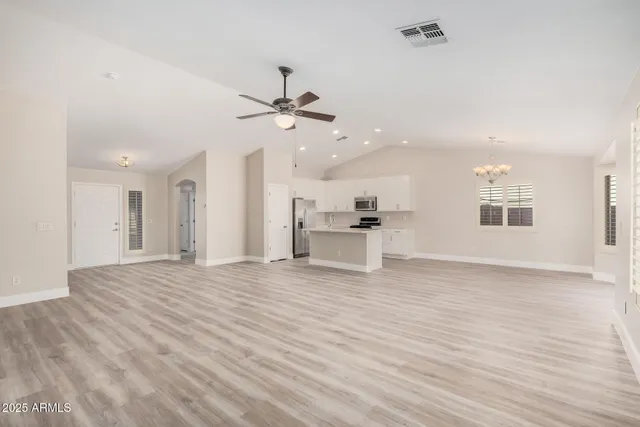 a view of an empty room with wooden floor and a kitchen