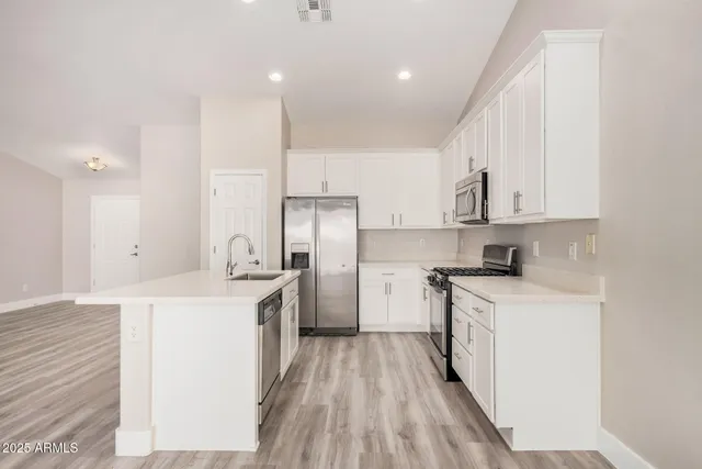 a kitchen with stainless steel appliances granite countertop a sink a stove a refrigerator and white cabinets with wooden floor