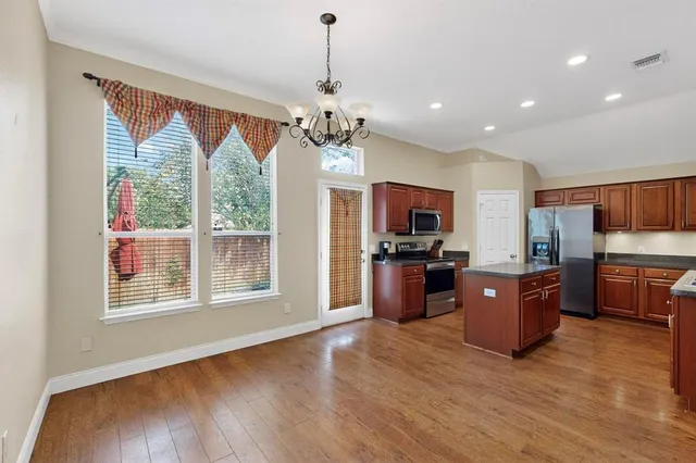 a large open kitchen with stainless steel appliances granite countertop a refrigerator oven a sink dishwasher a dining table and chairs with wooden floor