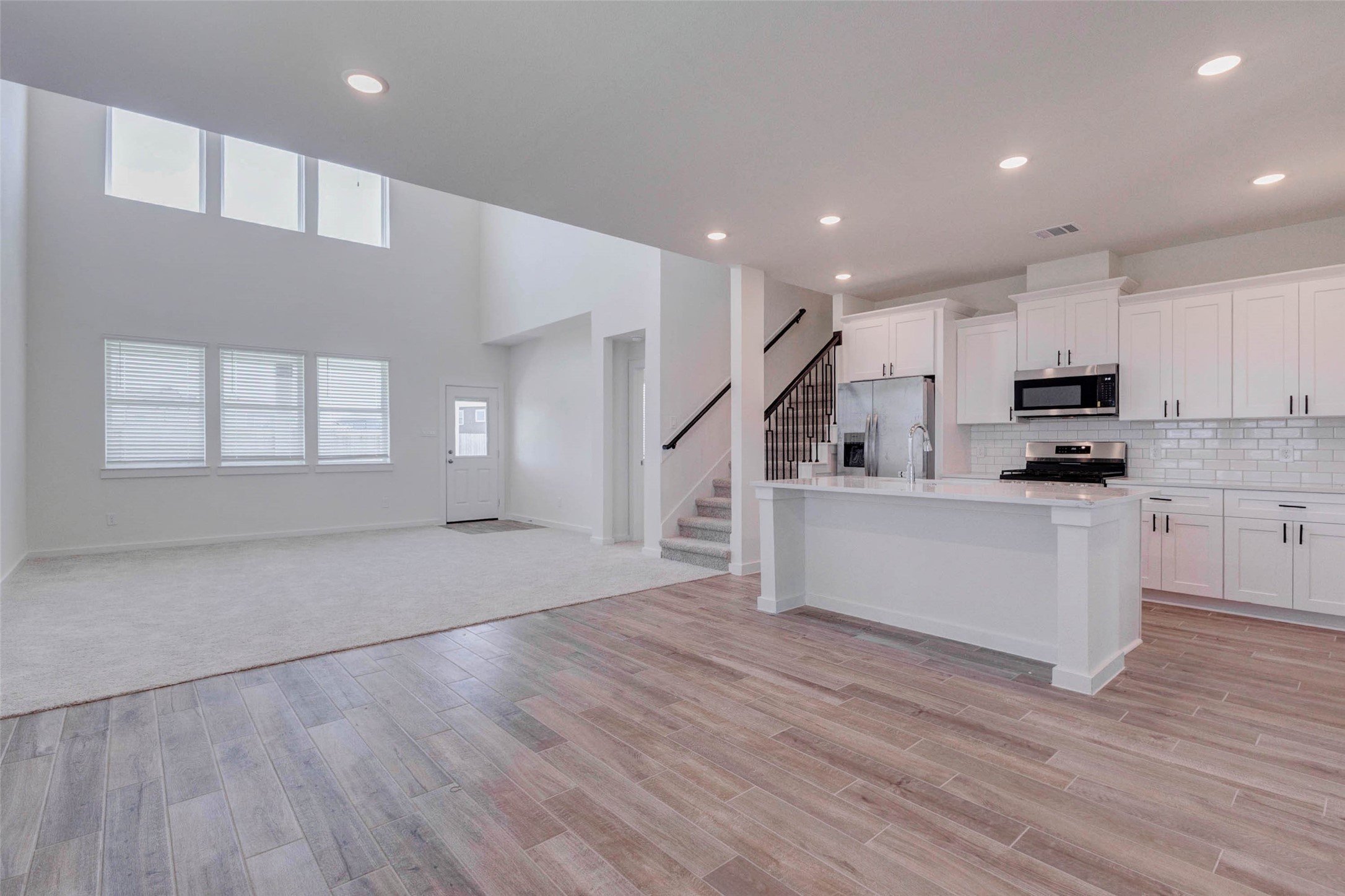 1206 Hemet Court Rosharon, TX 77583 - Photo 6 of 21 Bright open-concept view connecting the kitchen, breakfast area, family room, and staircase. The white kitchen cabinetry, large island, quartz-style surfaces, and subway tile backsplash create a fresh modern look. The family room features soaring ceilings, generous windows, and soft carpet, offering a comfortable gathering space at the center of the home.