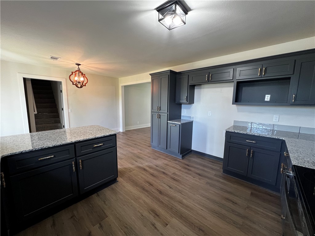 213 Carter Road Pottsville, AR 72858 - Photo 9 of 41 Kitchen featuring new dark cabinetry, speckled granite countertops, wood-finish LVP flooring, and a central eat-in island.