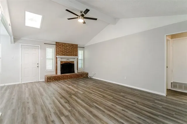 an empty room with wooden floor fireplace and windows
