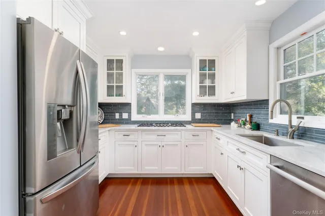a kitchen with stainless steel appliances granite countertop a refrigerator a sink and white cabinets with wooden floor
