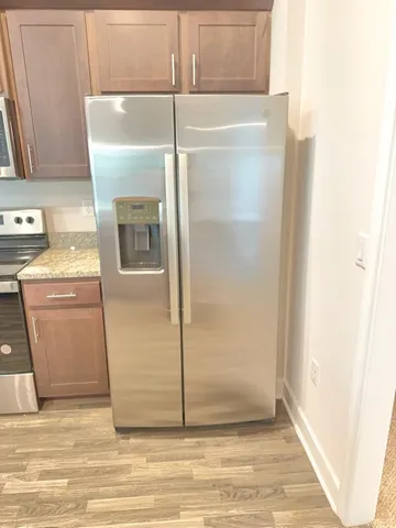 a view of a refrigerator in kitchen and an empty room with wooden floor