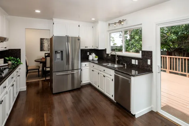 a kitchen with granite countertop a refrigerator a stove a sink cabinets and wooden floor