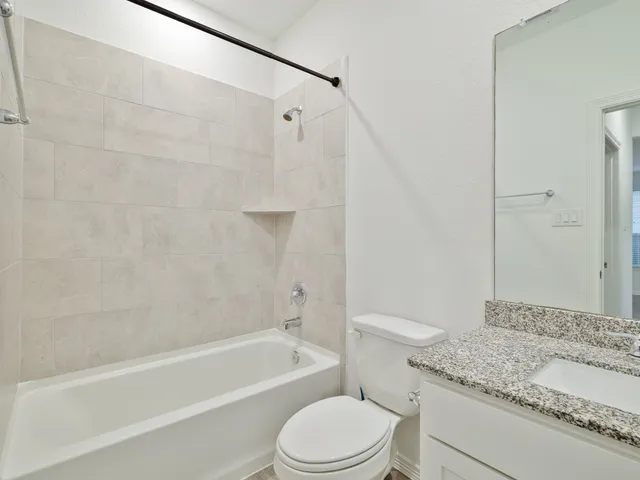 a bathroom with a granite countertop bathtub shower sink vanity and toilet