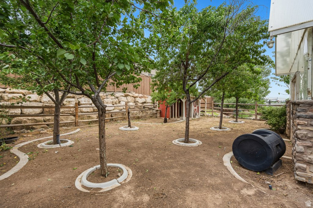 672 Perry Hollow Drive Mapleton, UT 84664 - Photo 101 of 106 Spacious yard area featuring multiple established trees with concrete tree rings, a natural stone retaining wall, and a rustic wooden fence
