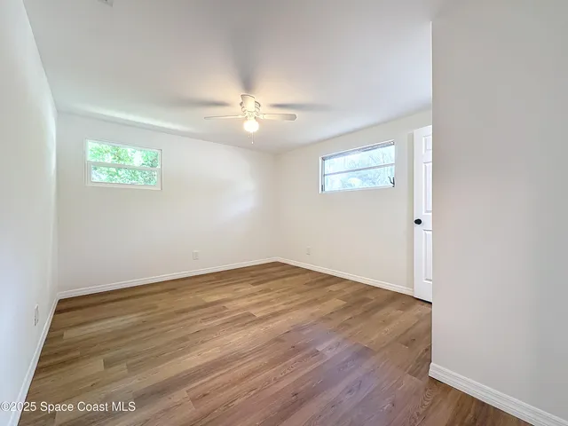 an empty room with wooden floor ceiling fan and windows