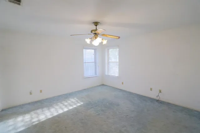 an empty room with chandelier fan and windows