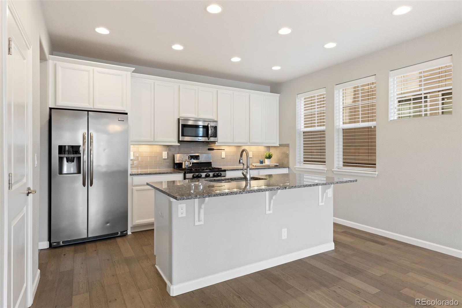 1338 Promontory Bluff View Colorado Springs, CO 80921 - Photo 4 of 28 a kitchen with stainless steel appliances granite countertop white cabinets a refrigerator a sink a stove a microwave and wooden floors