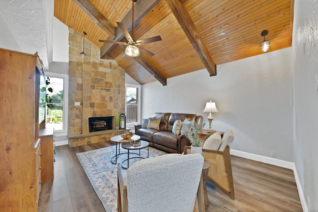 306 Rochelle Boulevard Irving, TX 75062 - Photo 7 of 40 Soaring vaulted wood ceiling with exposed beams and ceiling fan anchors the living space, while a stacked-stone fireplace with integrated hearth serves as a striking focal point