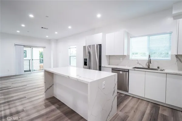 a kitchen with stainless steel appliances a sink a stove a refrigerator and island with wooden floor
