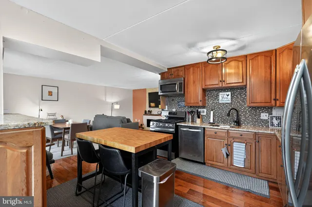 a kitchen with stainless steel appliances granite countertop a stove top oven a sink dishwasher a dining table and chairs with wooden floor