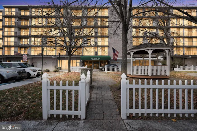 a front view of a building with large trees and plants