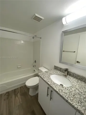a bathroom with a granite countertop sink a toilet a mirror and bathtub
