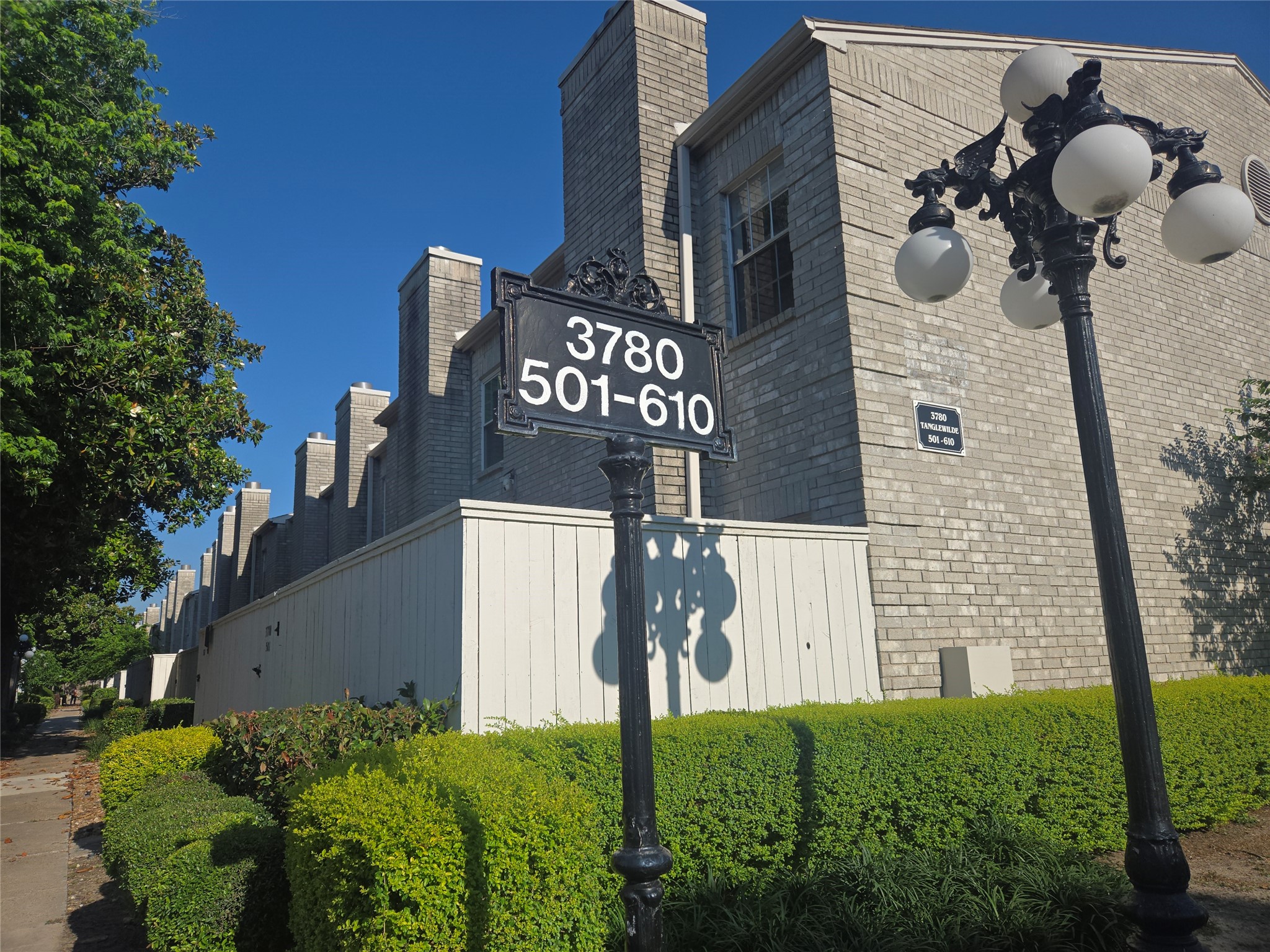 3780 Tanglewilde Street, Unit 501 Houston, TX 77063 - Photo 25 of 26 This photo shows a brick townhouse complex with a vintage-style lamp post. The building has multiple units, indicated by the address sign for units 501-610. There is a well-maintained path and neatly trimmed hedges, suggesting a tidy and organized community setting.