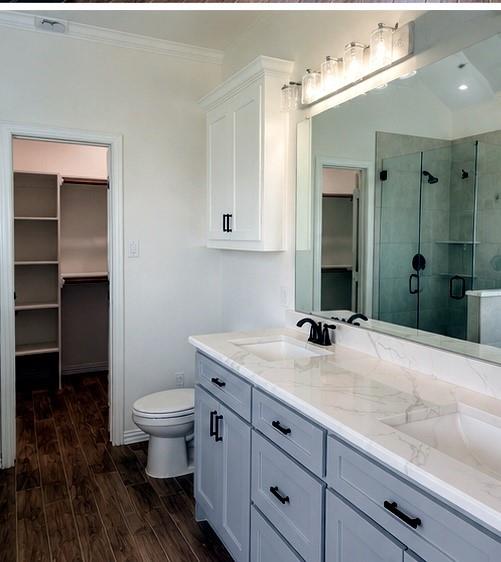 8008 County Road 1058 Rice, TX 75155 - Photo 7 of 12 Dual vanity with quartz countertops, wood-finish flooring, a glass-enclosed shower, a built-in wall cabinet, and a walk-in closet with shelving