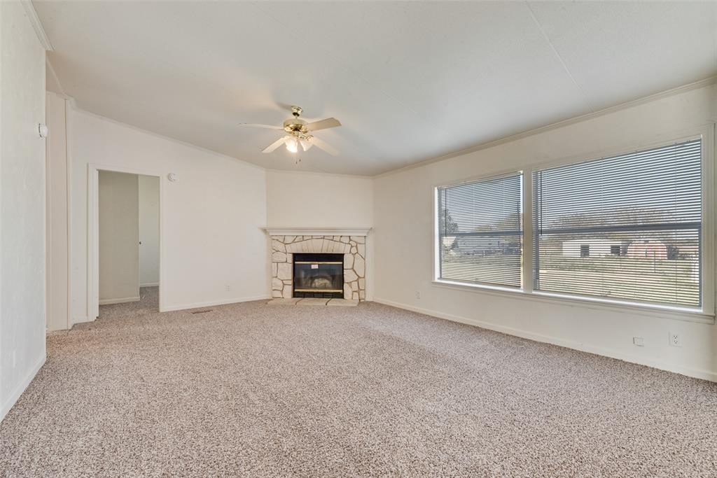 817 Kaufman Street Rosser, TX 75158 - Photo 8 of 29 Unfurnished living room with light colored carpet, a stone fireplace, crown molding, and ceiling fan