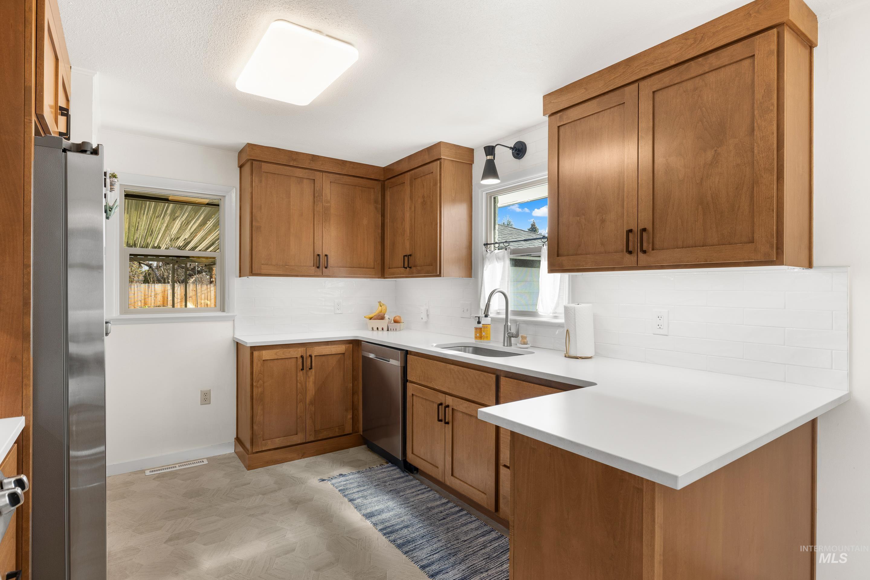 1010 Forrest Street Boise, ID 83705 - Photo 14 of 50 Kitchen with brown cabinetry, a peninsula, stainless steel appliances, backsplash, and light flooring