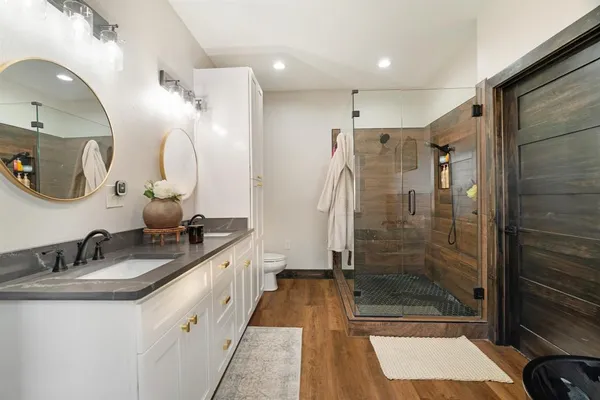 a bathroom with a double vanity sink a toilet a mirror and shower