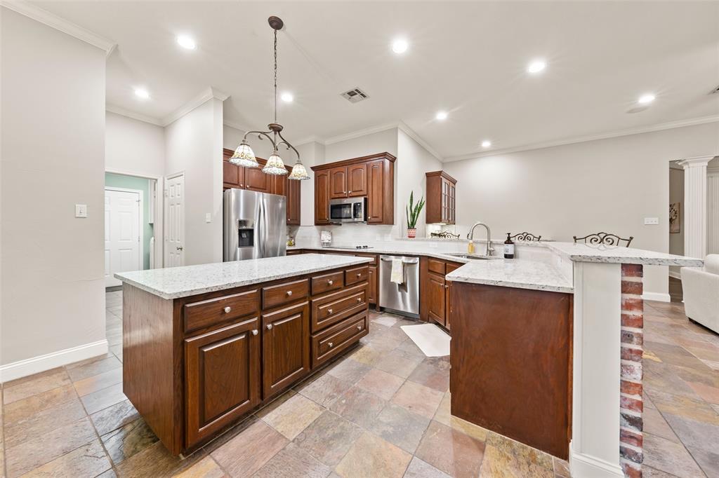 517 Chado Lane Robinson, TX 76706 - Photo 10 of 40 Kitchen with stainless steel appliances, a center island, a peninsula, stone tile flooring, and light stone counters
