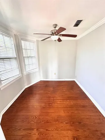 an empty room with wooden floor fan and windows