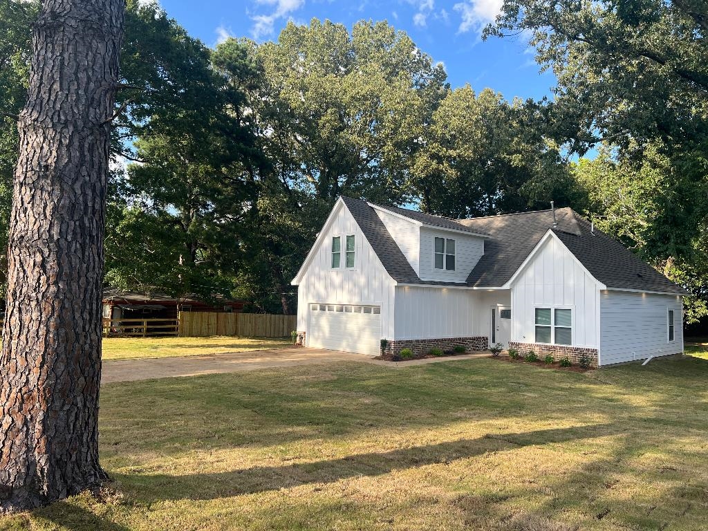 View of home's exterior with a shingled roof, driveway, a garage, stone siding, and view of scattered trees