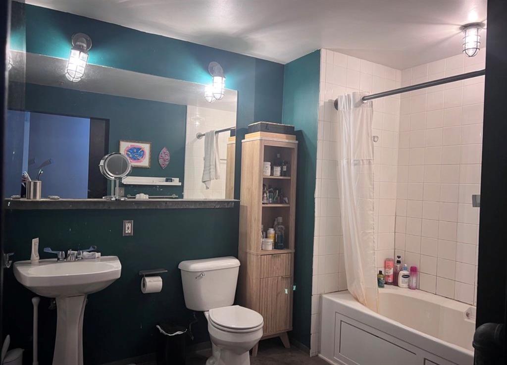 1122 Jackson Street, Unit 514 Dallas, TX 75202 - Photo 25 of 40 Bathroom featuring a pedestal sink, a toilet, a full-size bathtub with white tile surround, and a wall-mounted mirror with industrial-style lighting fixtures
