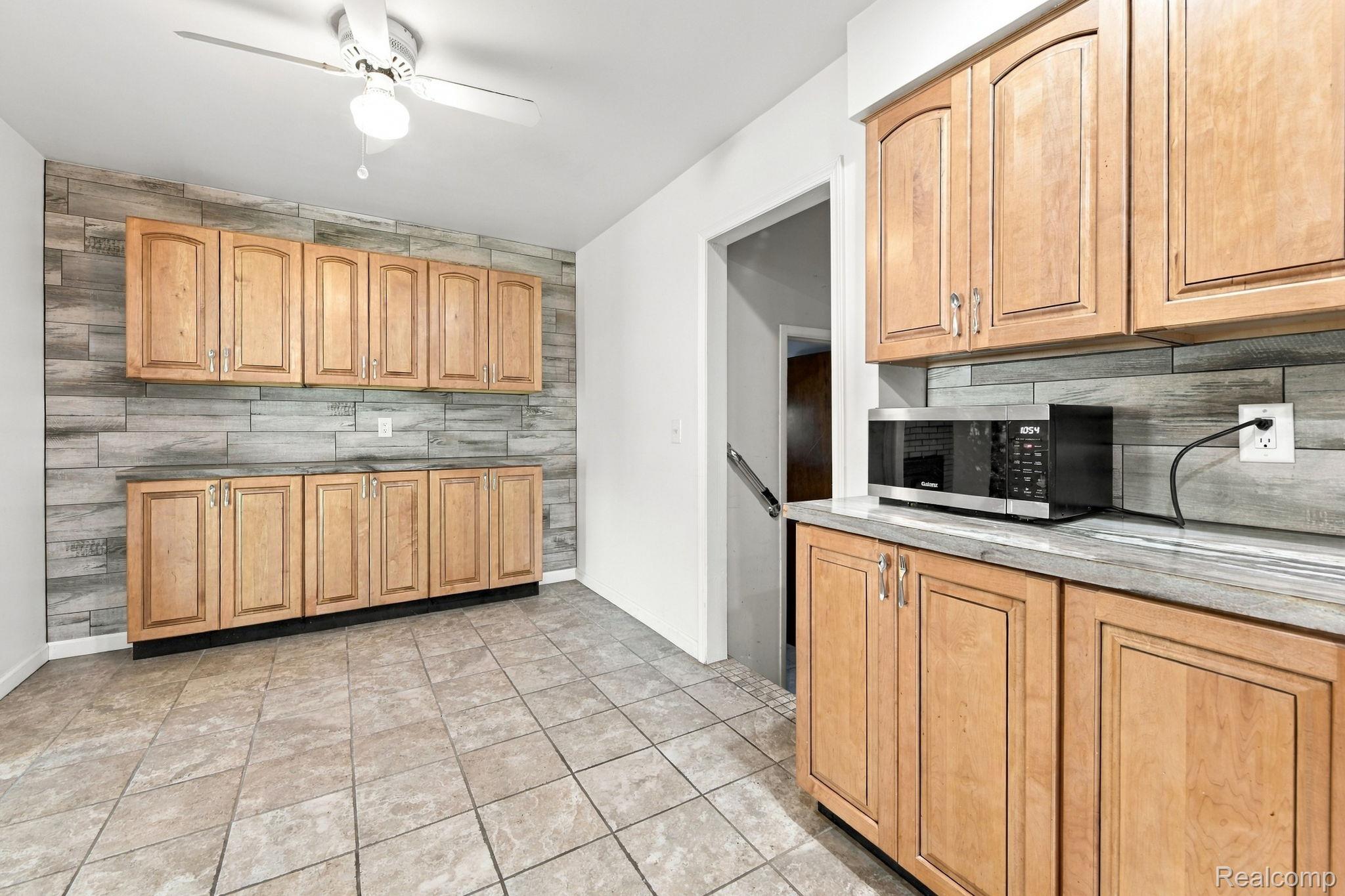 13265 12 Mile Road Warren, MI 48088 - Photo 20 of 33 Wood-finish cabinetry with silver-tone hardware, tile flooring, wood-look plank accent wall, and a ceiling fan