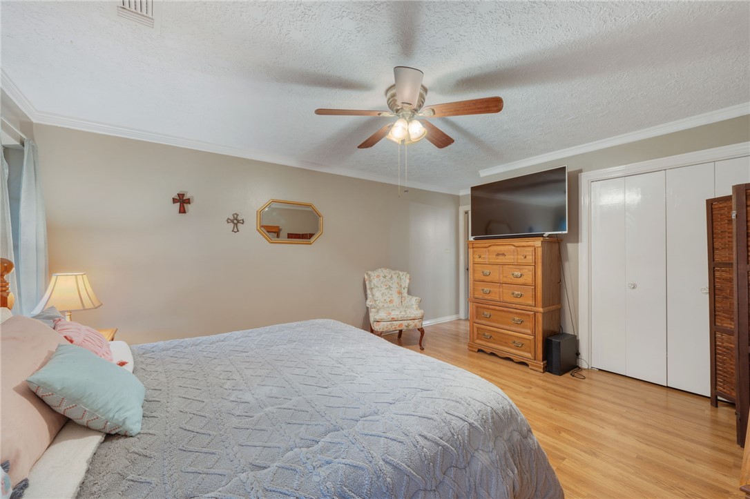503 Calvert Street Hearne, TX 77859 - Photo 12 of 30 Bedroom featuring light wood-type flooring, a textured ceiling, a closet, crown molding, and ceiling fan