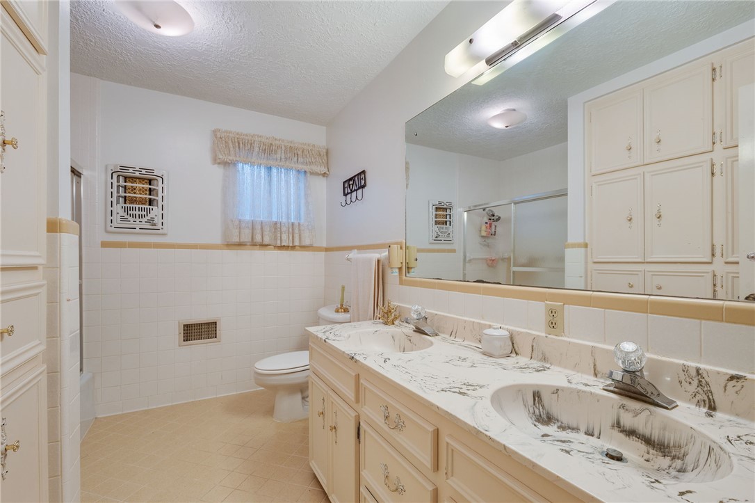 503 Calvert Street Hearne, TX 77859 - Photo 20 of 30 Bathroom with a textured ceiling, double vanity, tile walls, light tile patterned flooring, and wainscoting
