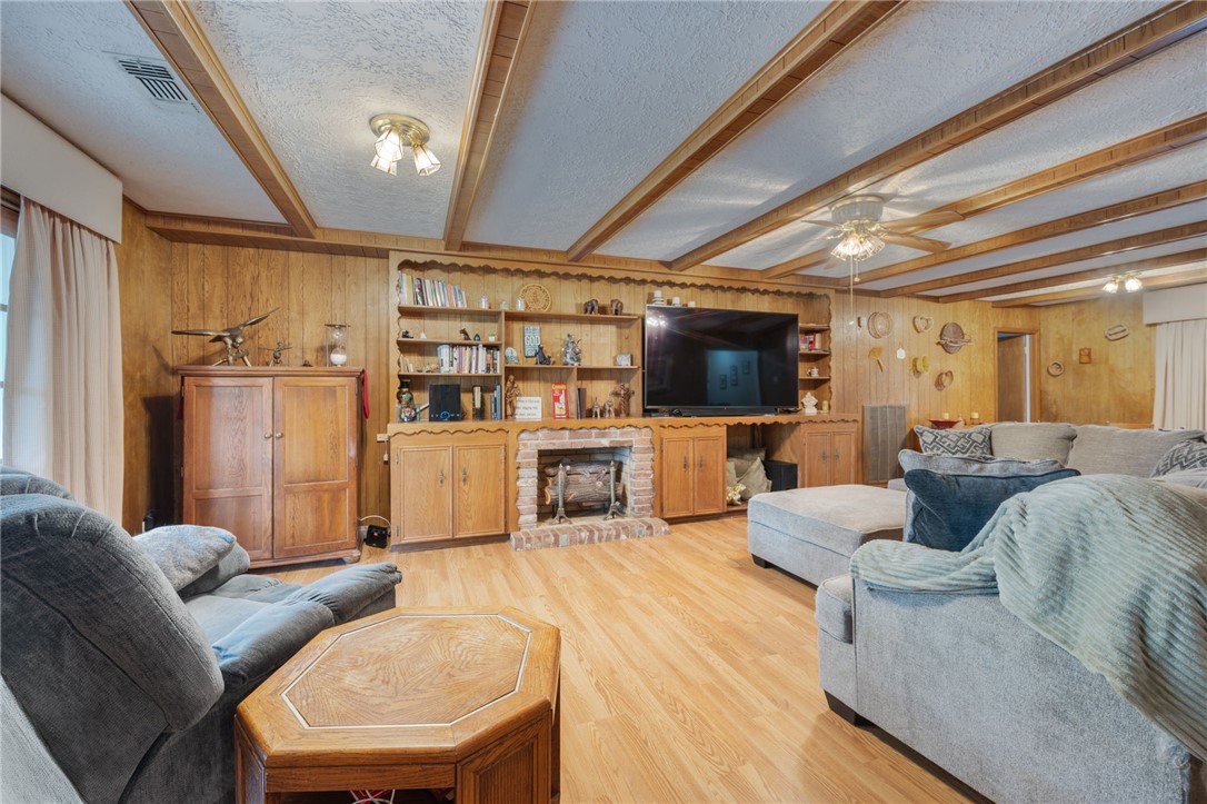 503 Calvert Street Hearne, TX 77859 - Photo 29 of 30 Living room featuring wood walls, beamed ceiling, light wood-style floors, a textured ceiling, and ceiling fan